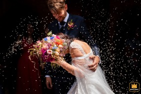 A Trieste, in Italia, gli sposi condividono un momento tenero mentre lei si protegge dal lancio del riso con il suo bouquet, su uno sfondo scuro.